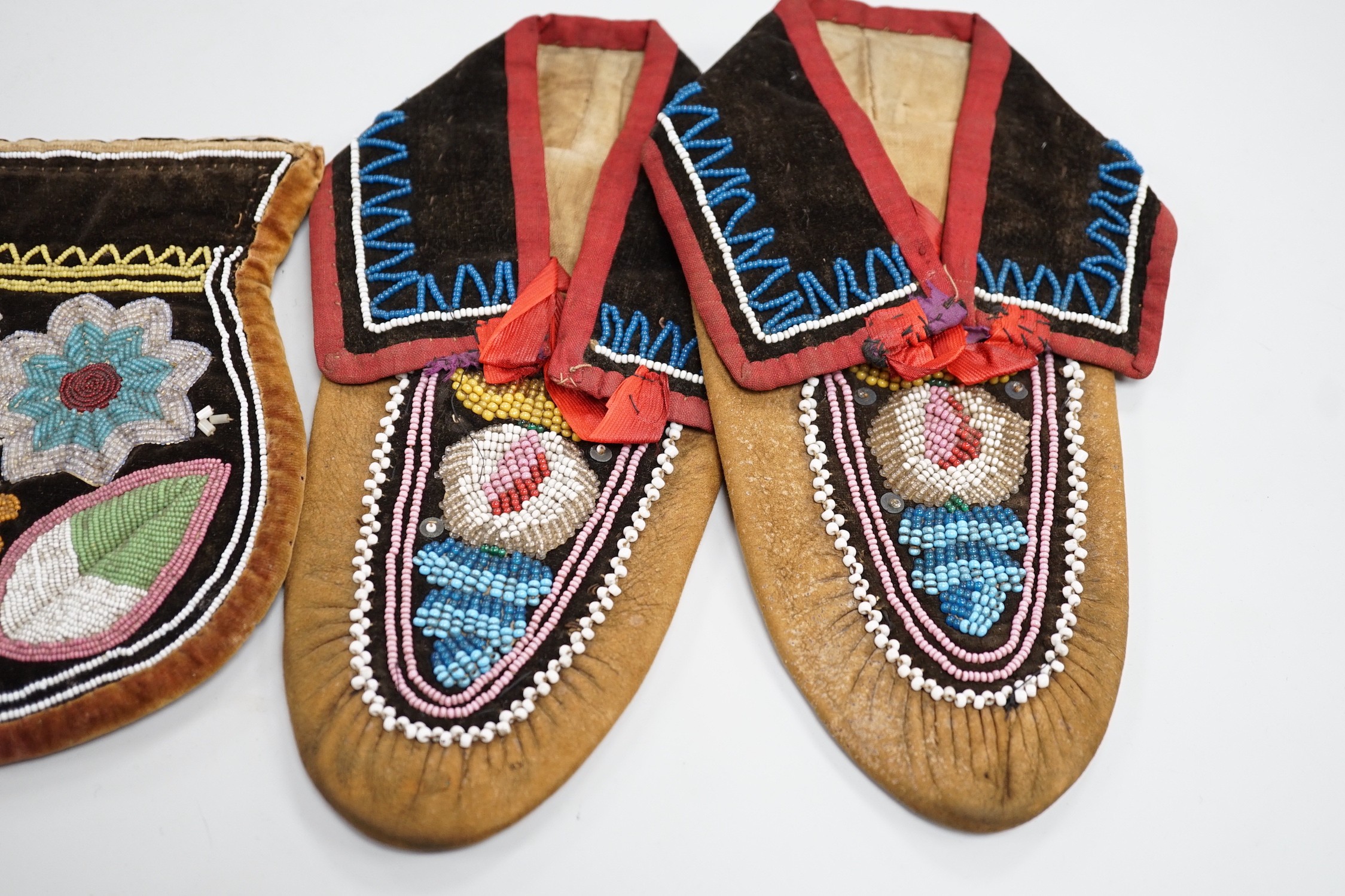 A pair of mid to late 19th century Mikmaq, North American Indian, moccasins, worked in floral beadwork on vamp, with velvet cuffs and red silk ties, together with two Wabanaki floral bead-worked velvet bags